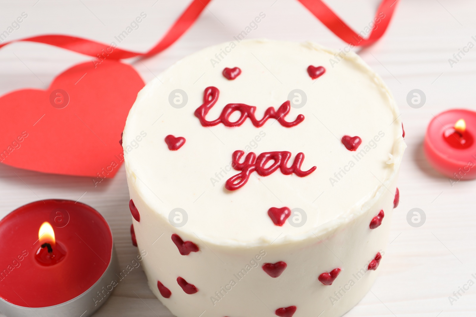 Photo of Bento cake with text Love You, candles and paper heart on white wooden table, closeup. St. Valentine's day surprise