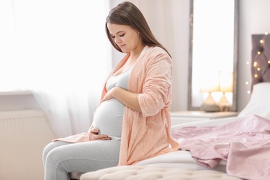 Photo of Beautiful pregnant woman sitting on bed at home