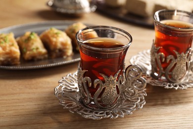 Photo of Glasses of traditional Turkish tea in vintage holders and fresh baklava on wooden table, closeup