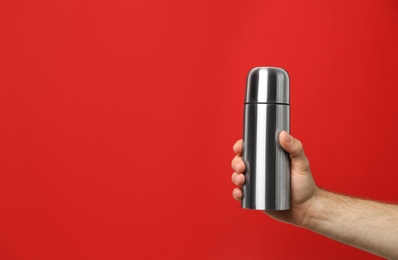 Man holding silver thermos on red background, closeup. Space for text