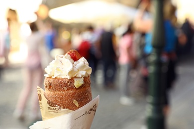 Photo of PRAGUE, CZECH REPUBLIC - APRIL 25, 2019: Traditional dessert trdelnik with whipped cream on city street, closeup. Space for text