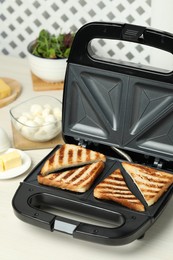 Modern sandwich maker with bread slices on white table