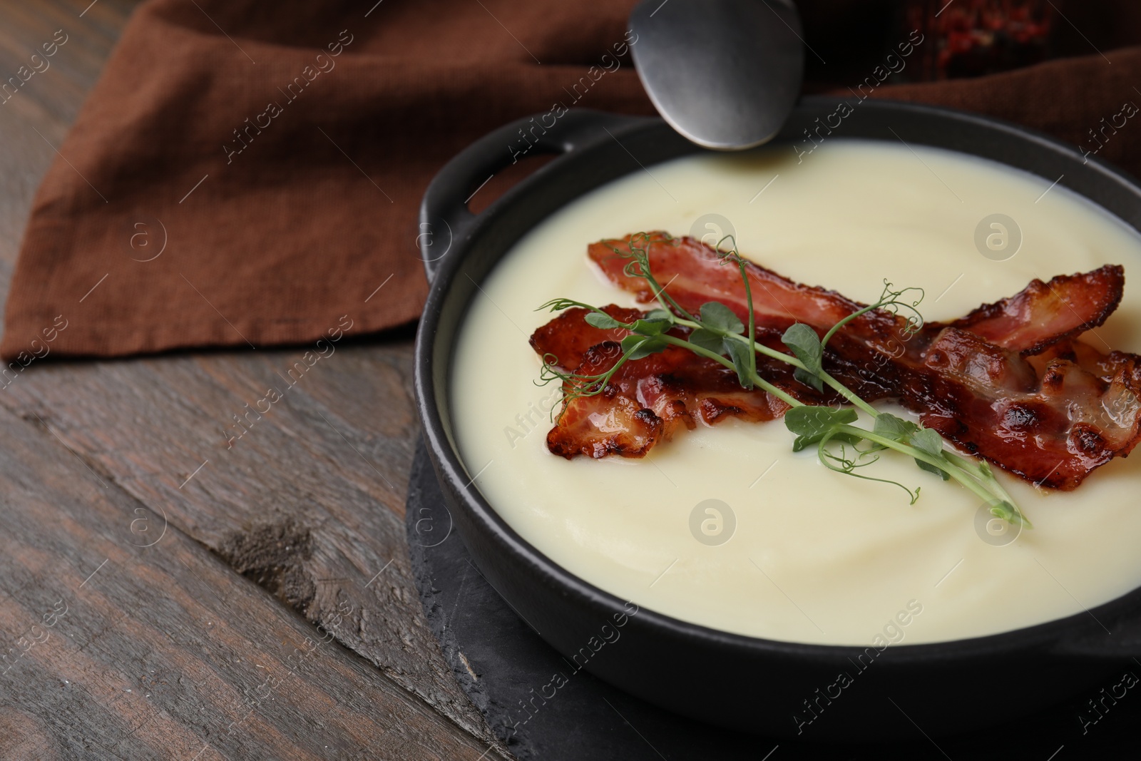 Photo of Delicious potato soup with bacon and microgreens in bowl on wooden table, closeup. Space for text