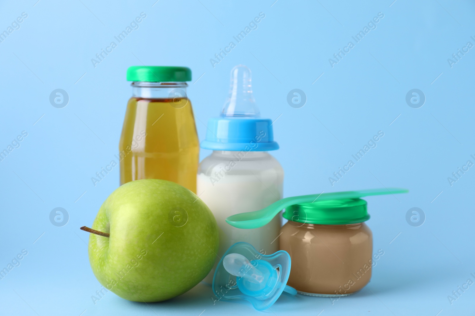 Photo of Healthy baby food, juice, milk, apple, spoon and pacifier on light blue background