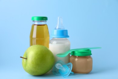 Photo of Healthy baby food, juice, milk, apple, spoon and pacifier on light blue background