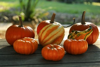 Many whole ripe pumpkins on wooden table outdoors