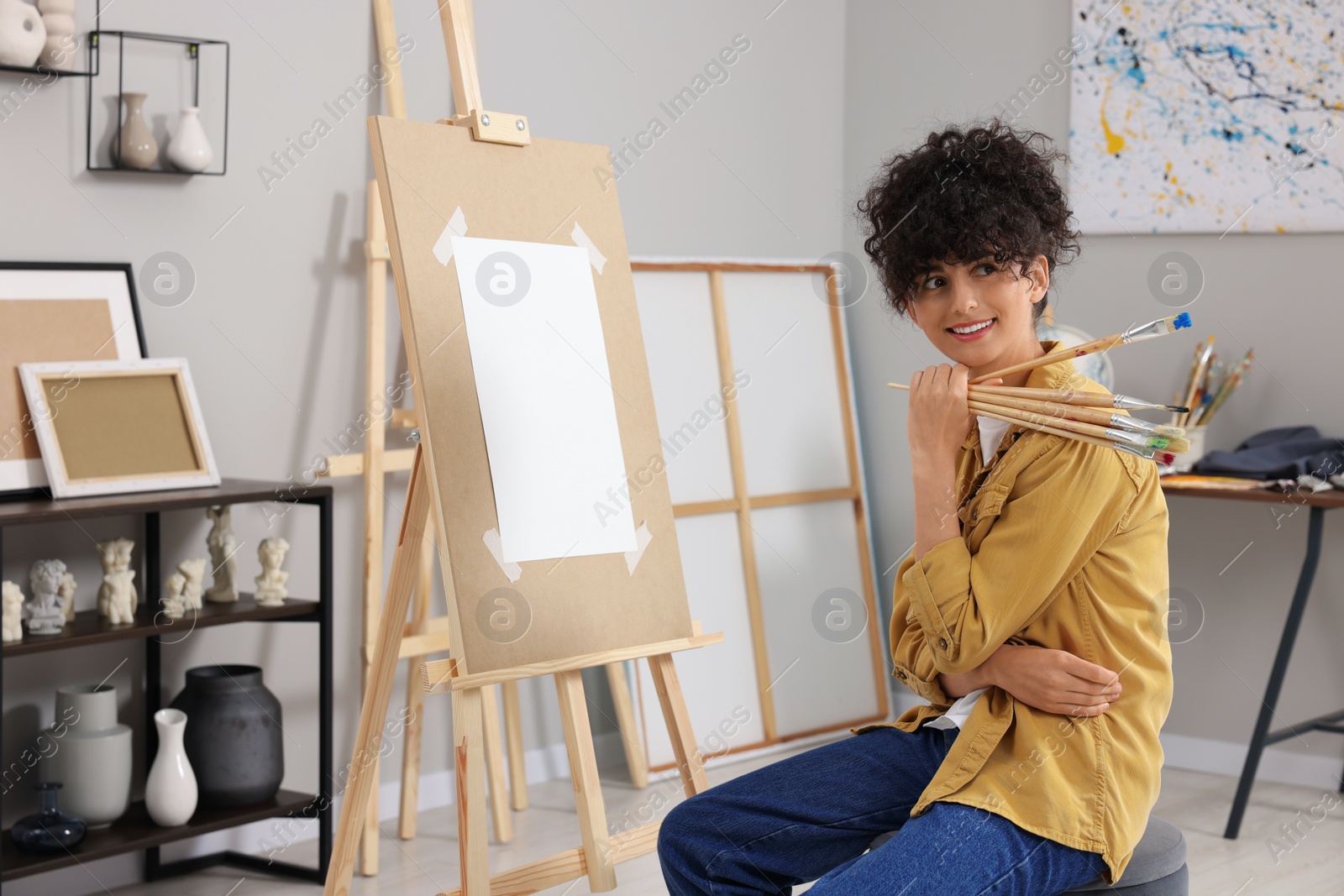 Photo of Happy woman with brushes near easel in studio