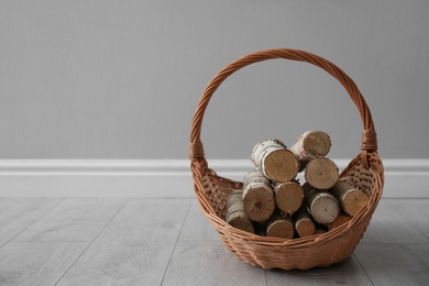 Wicker basket with firewood near grey wall indoors, space for text