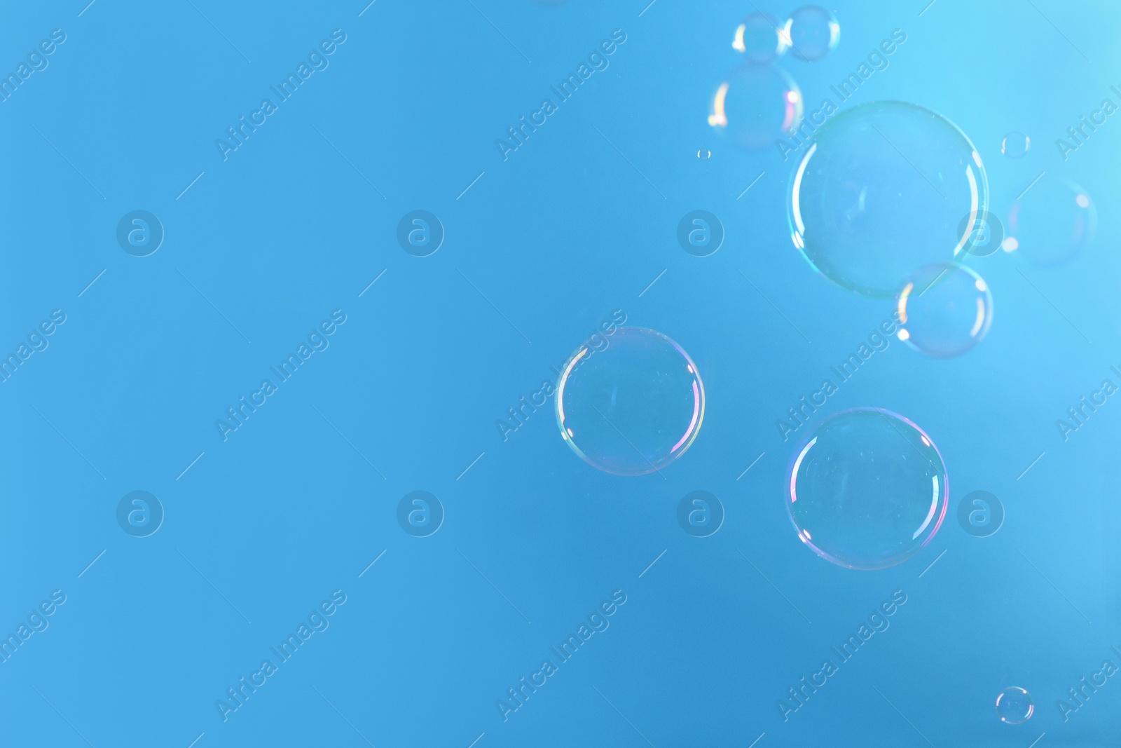 Photo of Beautiful transparent soap bubbles on light blue background, space for text