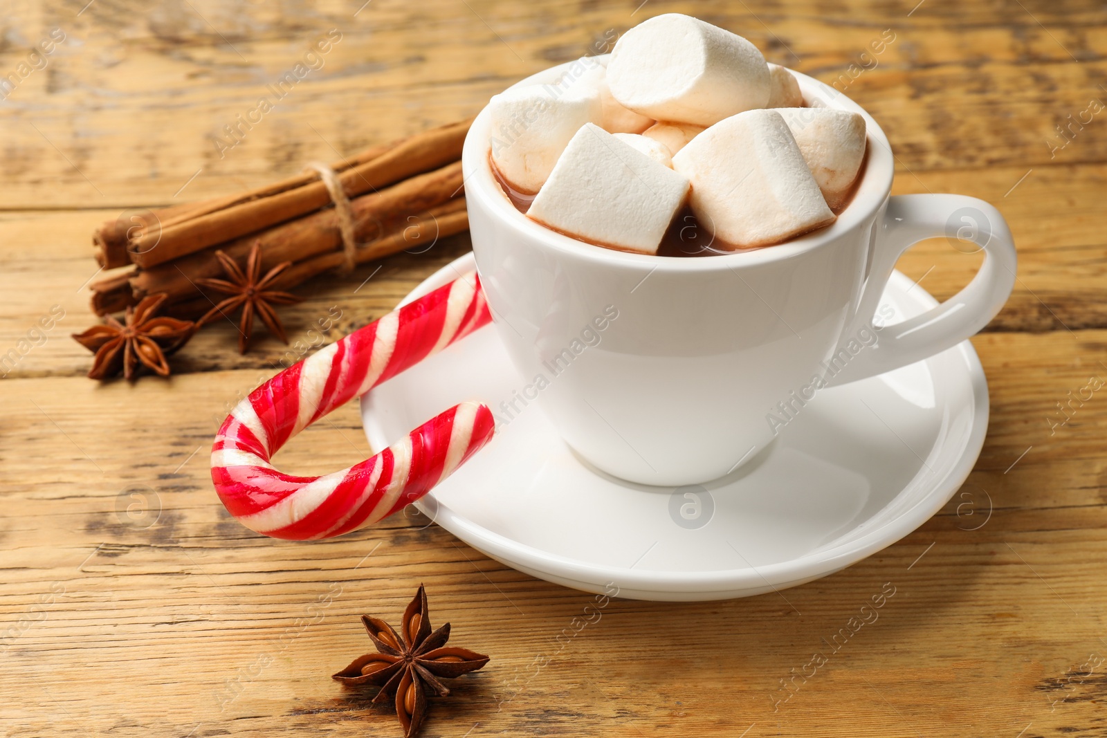 Photo of Tasty hot chocolate with marshmallows, candy cane and spices on wooden table, closeup