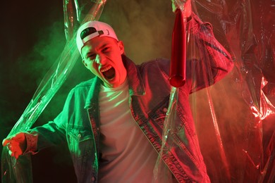 Young man with baseball bat on color background in neon lights