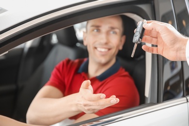 Salesman passing key to young man in auto at dealership. Buying new car