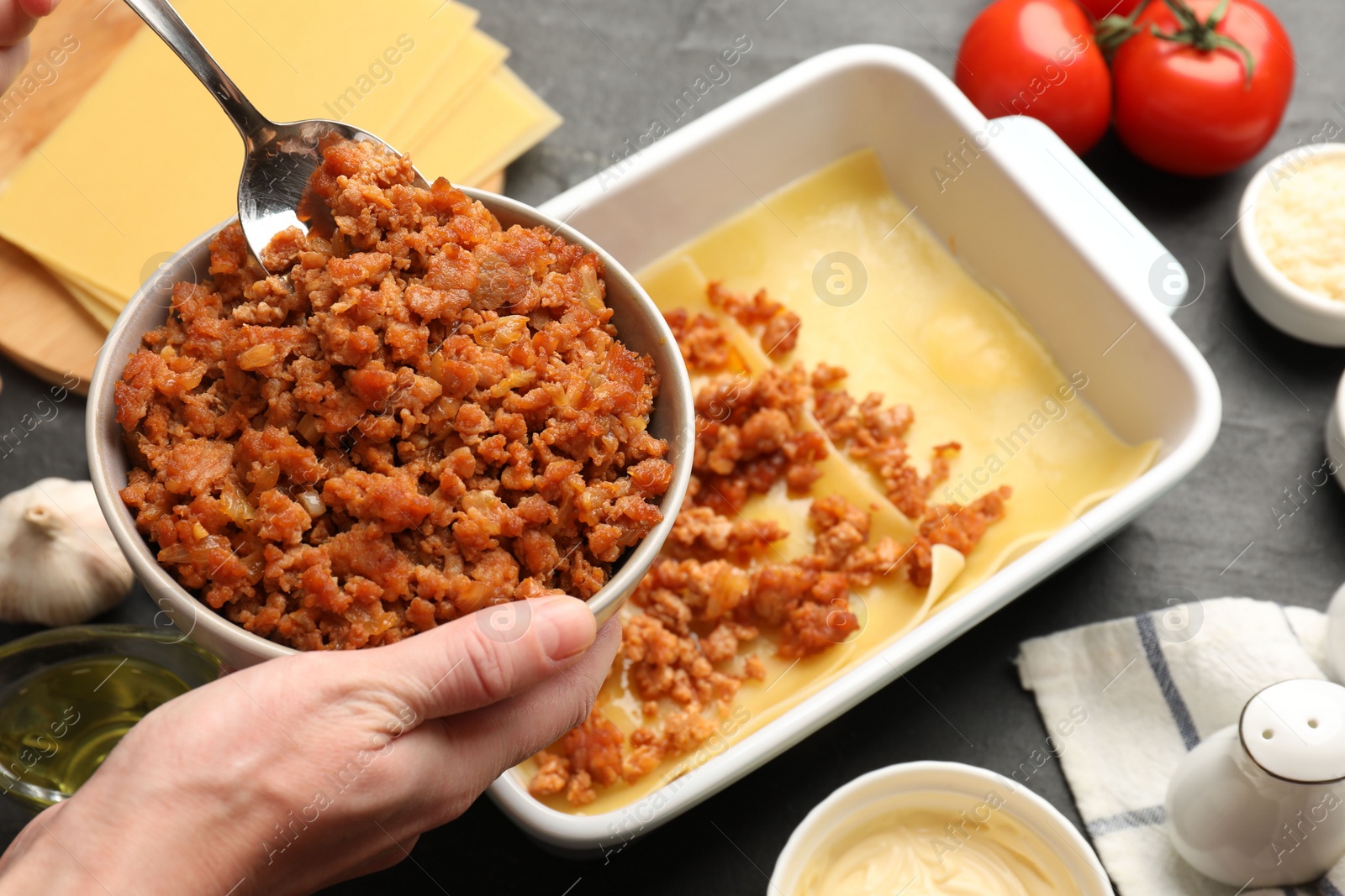 Photo of Woman making lasagna at dark table, closeup