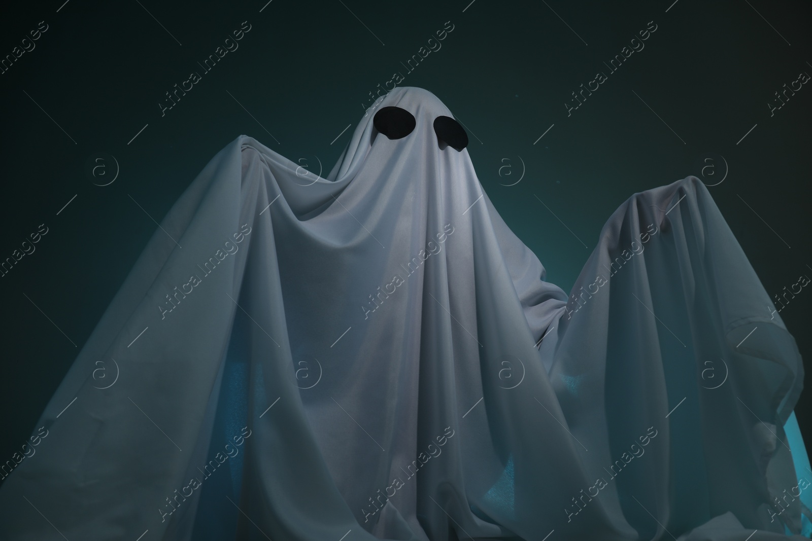 Photo of Creepy ghost. Woman covered with sheet on dark teal background