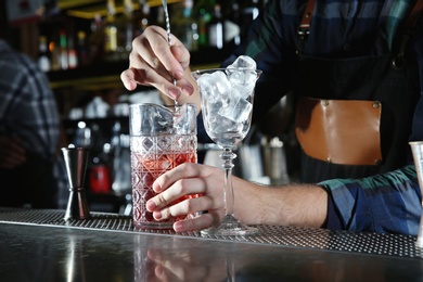 Photo of Barman mixing alcoholic cocktail at counter in night club, closeup