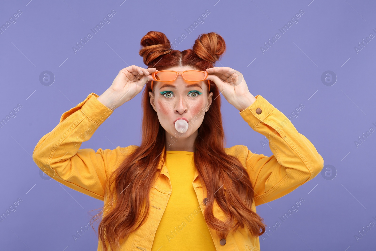 Photo of Portrait of surprised woman with bright makeup blowing bubble gum on violet background