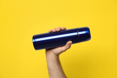 Photo of Man holding blue thermos on yellow background, closeup