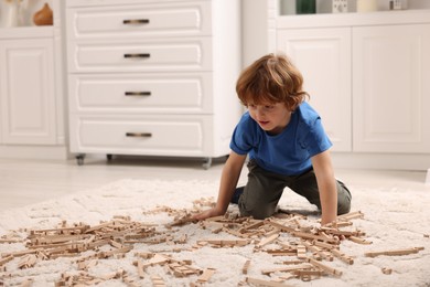 Cute little boy playing with wooden construction set on carpet at home, space for text. Child's toy