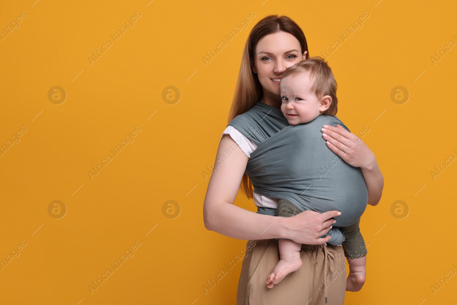 Photo of Mother holding her child in baby wrap on orange background. Space for text