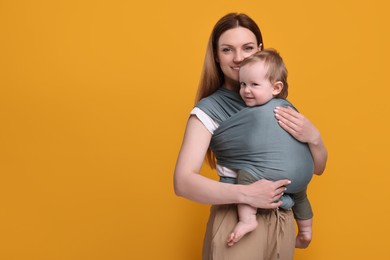 Photo of Mother holding her child in baby wrap on orange background. Space for text