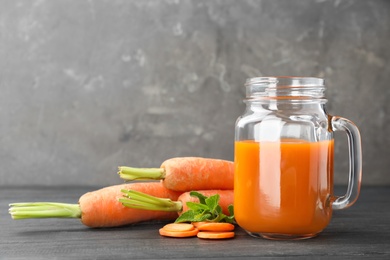 Mason jar of tasty drink and carrots on wooden table against color background, space for text