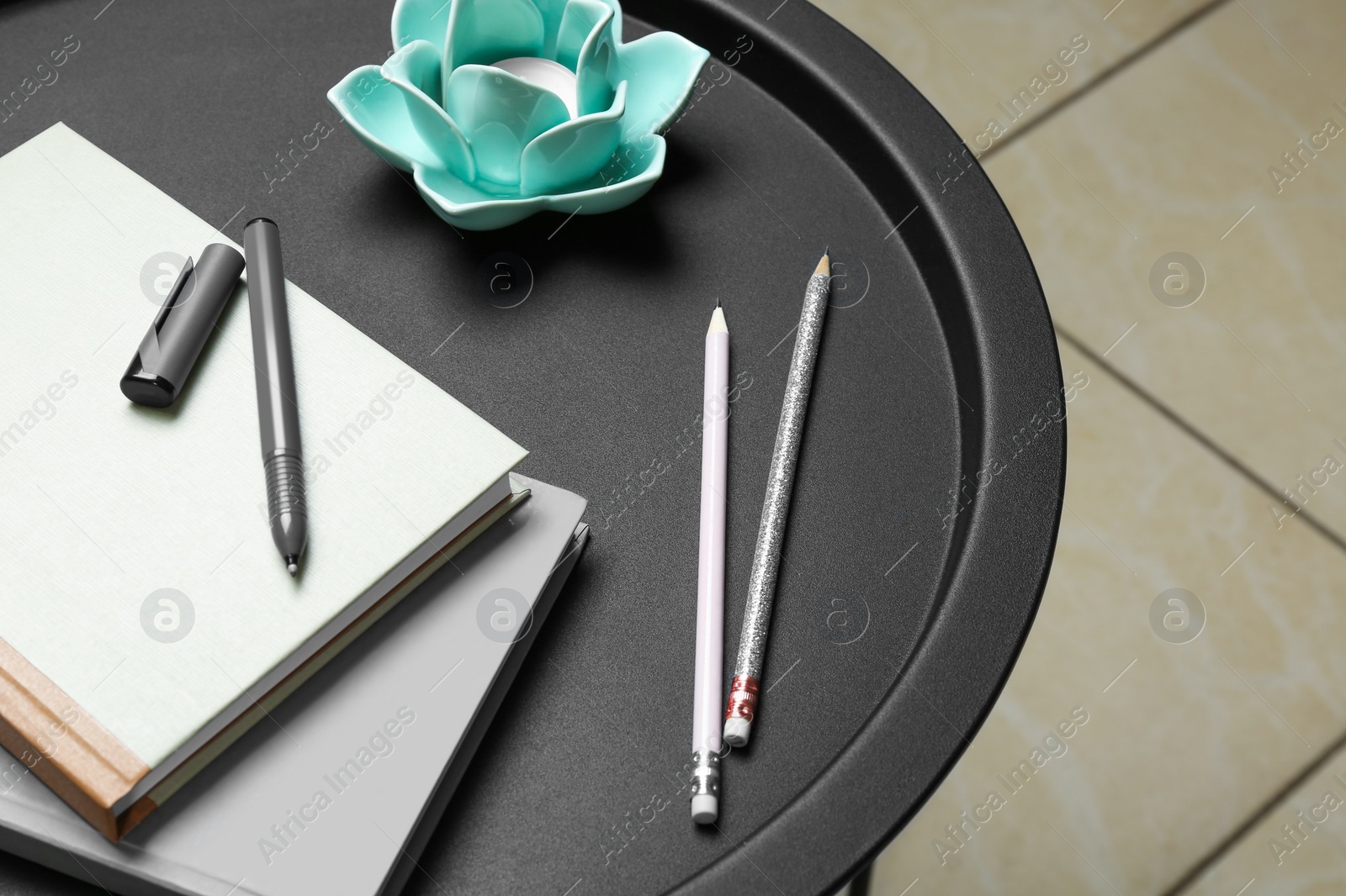 Photo of Notebooks, pen, pencils and decorative holder with candle on round table indoors, closeup