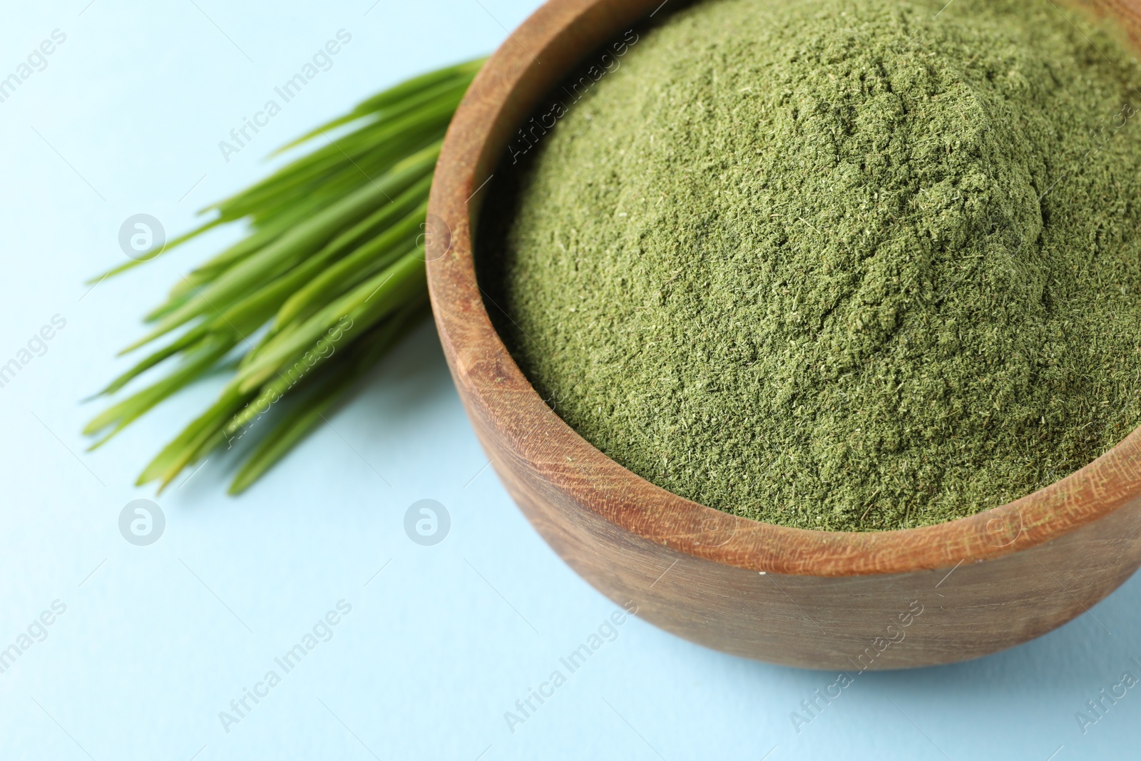 Photo of Wheat grass powder in bowl and fresh sprouts on light blue background, closeup