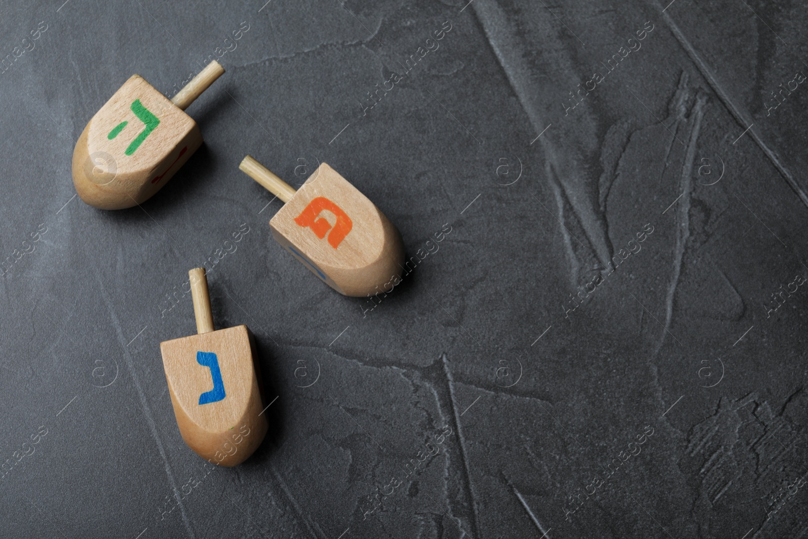 Photo of Hanukkah traditional dreidels on grey table. Space for text