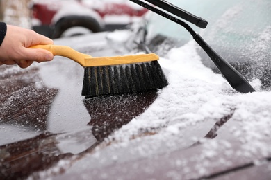 Photo of Man cleaning car hood from snow with brush outdoors, closeup
