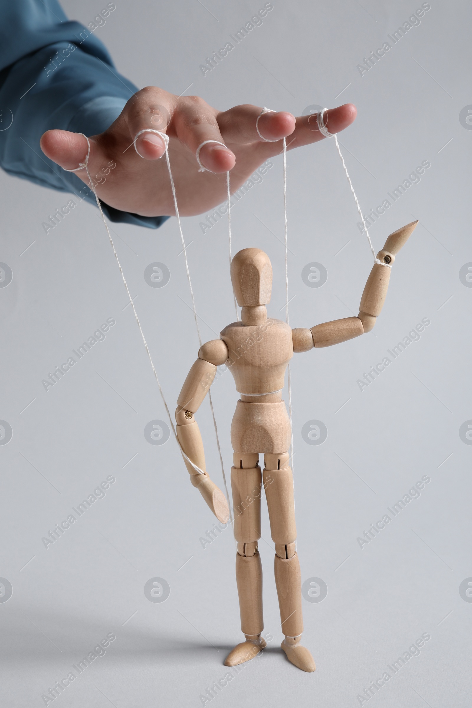 Photo of Woman pulling strings of puppet on light grey background, closeup