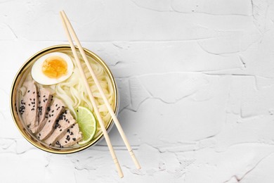 Photo of Bowl of delicious rice noodle soup with meat and egg on white textured table, top view. Space for text