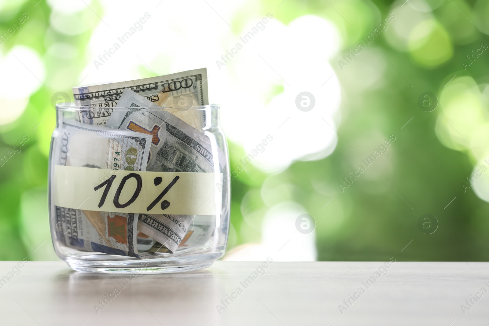 Photo of Glass jar with money and label 10 PERCENT on table against blurred background. Space for text