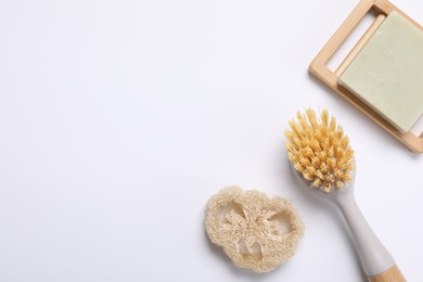 Photo of Cleaning brush, soap bar and loofah on white background, flat lay. Space for text