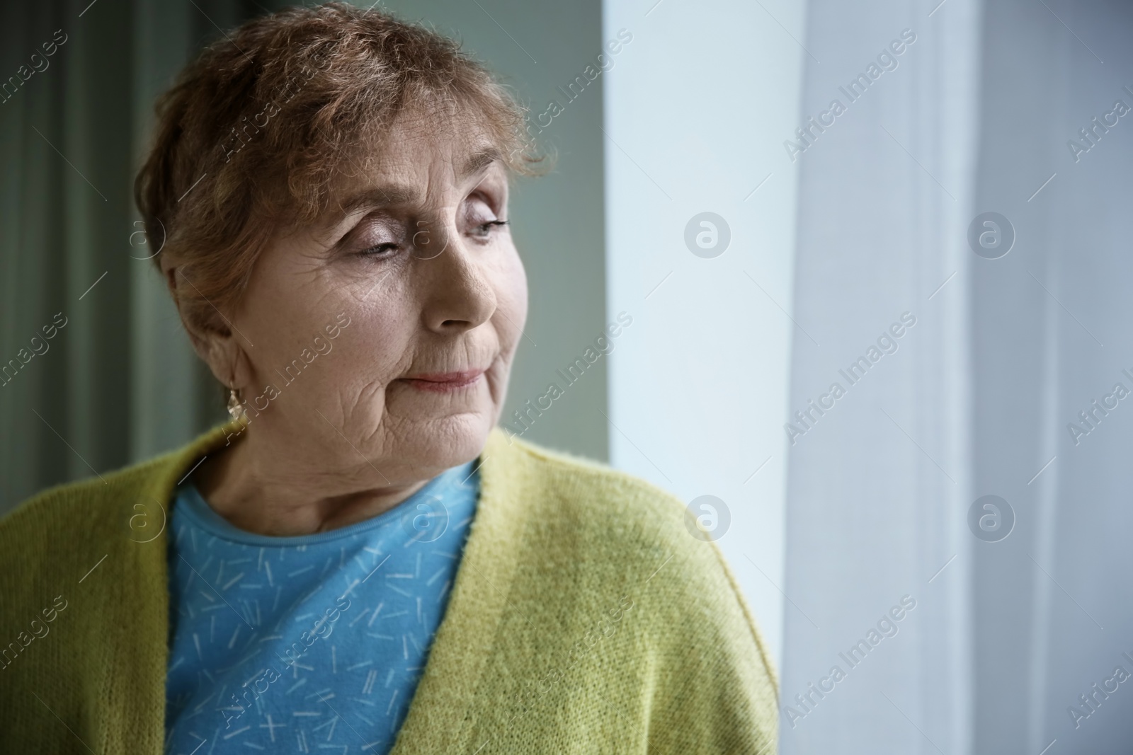Photo of Portrait of elderly woman near window indoors. Space for text