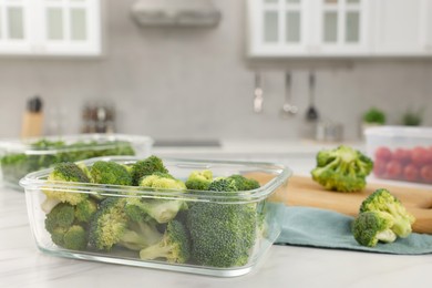 Glass container with fresh broccoli on white marble table, closeup and space for text. Food storage