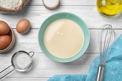 Batter for thin pancakes and products on white wooden table, flat lay