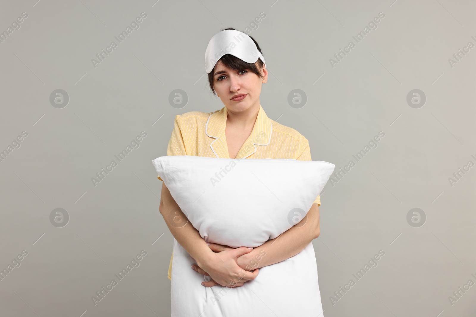 Photo of Woman in pyjama and sleep mask holding pillow on grey background