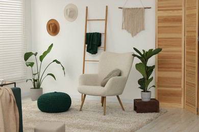 Photo of Comfortable armchair, pouf and houseplants in stylish room. Interior design