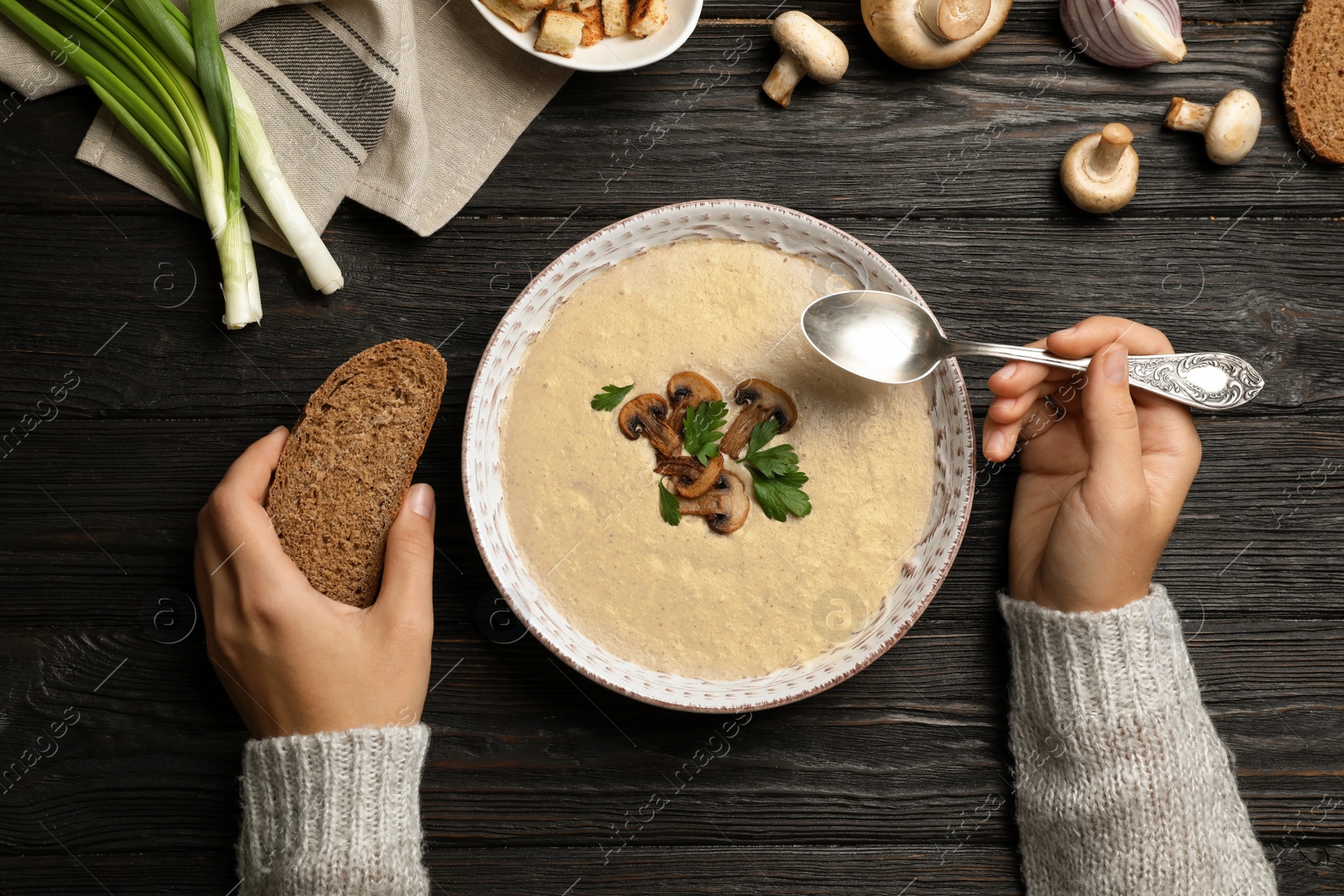 Photo of Woman eating fresh homemade mushroom soup from bowl on table, top view