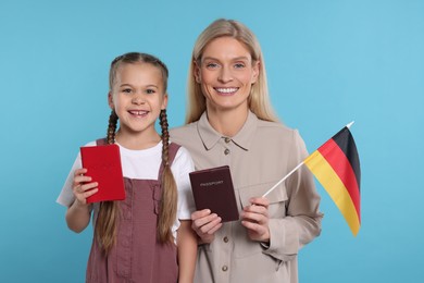 Photo of Immigration. Happy woman with her daughter holding passports and flag of Germany on light blue background