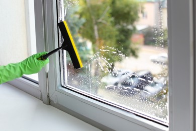 Woman cleaning glass with squeegee indoors, closeup