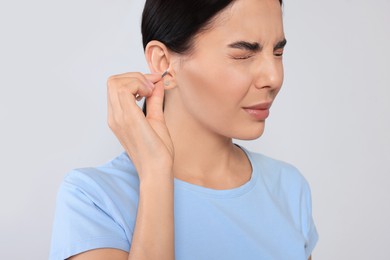 Photo of Young woman cleaning ear with cotton swab on light grey background, closeup