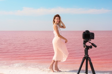 Photo of Young woman posing in front of professional camera near pink lake on sunny day