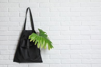 Photo of Eco tote bag with leaf hanging on white brick wall. Space for text