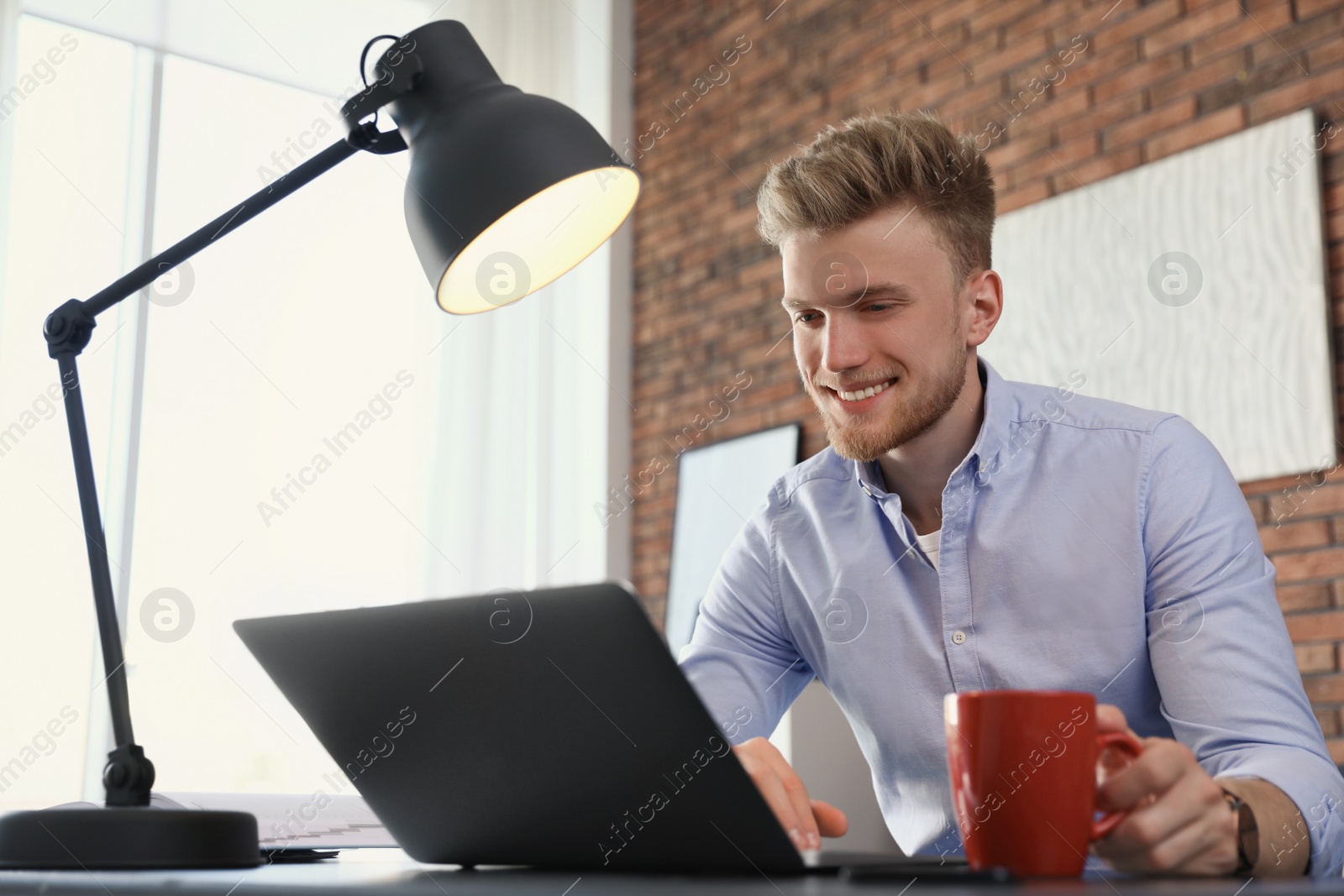 Photo of Young man using laptop at table indoors