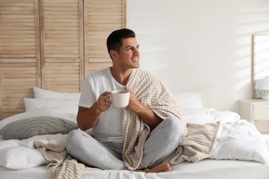 Photo of Man covered with plaid enjoying hot morning drink on bed indoors