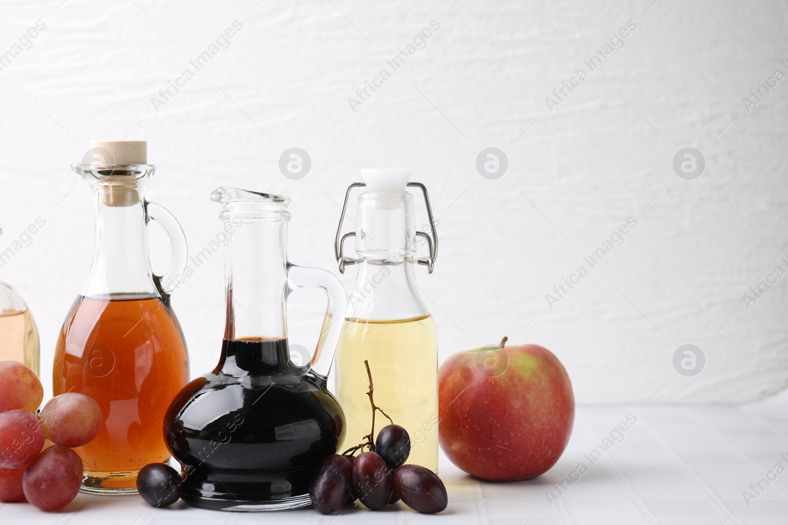 Photo of Different types of vinegar and ingredients on light tiled table, closeup. Space for text