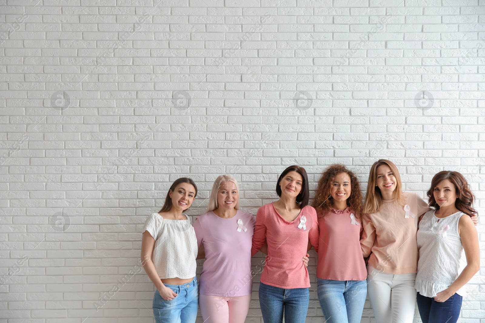 Photo of Group of women with silk ribbons near brick wall, space for text. Breast cancer awareness concept