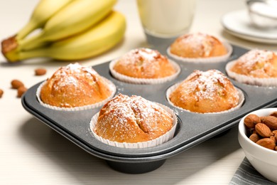 Photo of Tasty homemade banana muffins powdered with sugar in tray on white wooden table, closeup