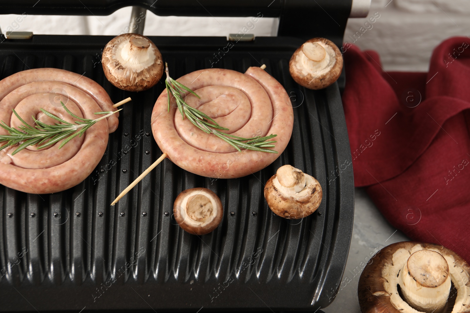 Photo of Electric grill with homemade sausages, rosemary and mushrooms on light table